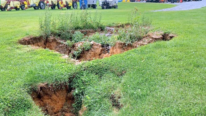 The ground has collapsed in a grassy area outdoors. Rocks and dirt falling from the sides have fallen into the middle.