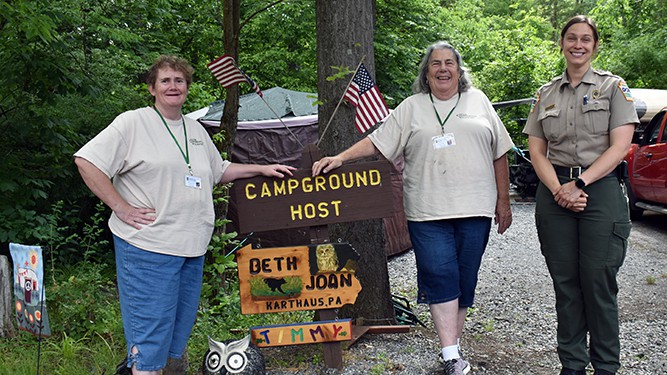 Beth Lerew and her daughter Joan stand next to their Campground Host sign with Gifford Pinchot State Park Manager Jennifer Park.