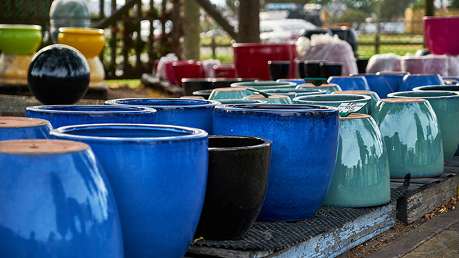 Large, glazed flowerpots in bright colors lined up on table outside
