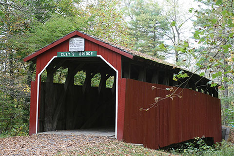 A covered bridge with a sign that says Clays Bridge.