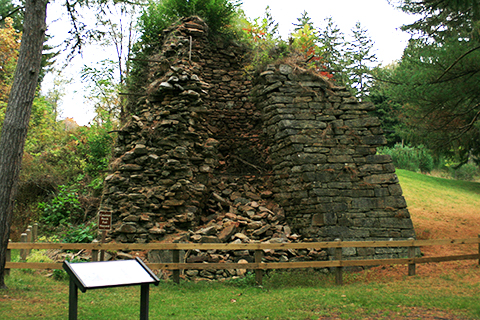 A crumbling, pryamid stone structure outdoors, An informational sign stands in front
