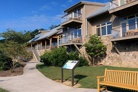 A bench and an exhibit are in front of a hotel with many porches which is the Nature Inn at Bald Eagle State Park.