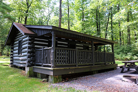 A log cabin with a porch is in the forest at Black Moshannon State Park.