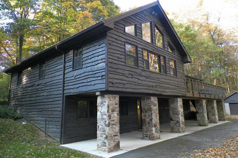 An impressive wainy wood sided building with large windows and a porch is in the forest at Laurel Hill State Park.