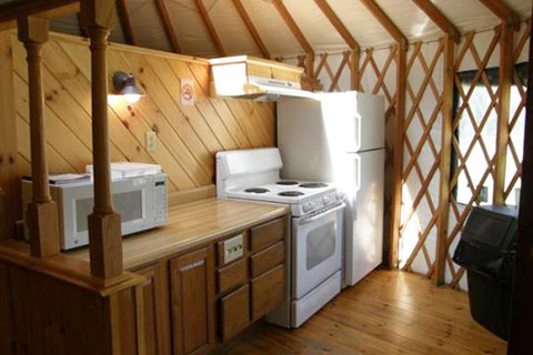 A counter, microwave oven, stove, and refrigerator are in a wooden room in a yurt at Little Pine State Park.