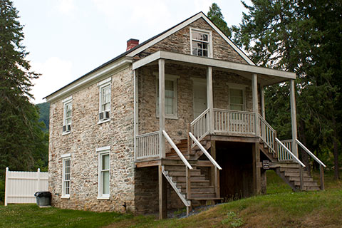 A historic, stone house has multiple staircases and a small porch at Pine Grove Furnace State Park.