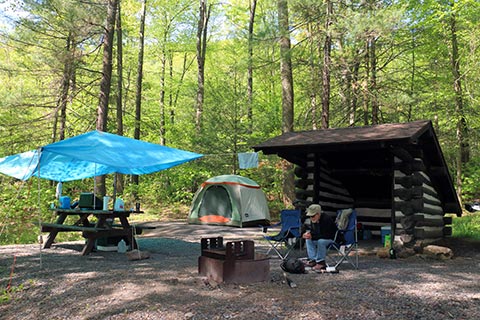 A camper sits by a campfire in front of a tent and an Adirondack shelter at Poe Paddy State Park.