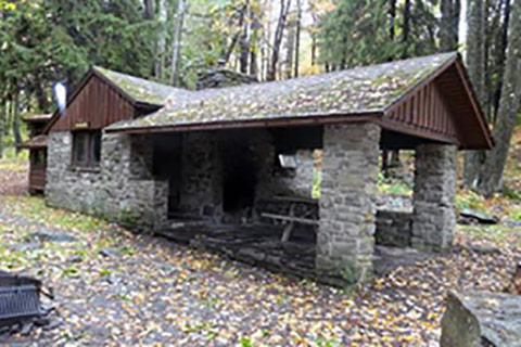 A cozy stone, rustic cabin is dappled with autumn-colored leaves at Promised Land State Park.