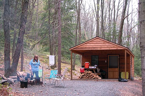 A camper enjoys a campfire outside of a cozy log cabin at Raymond B Winter State Park.