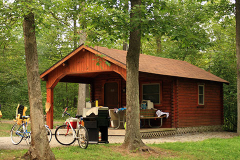 Bikes and a grill sit in front of a cozy log cabin at Shawnee State Park.