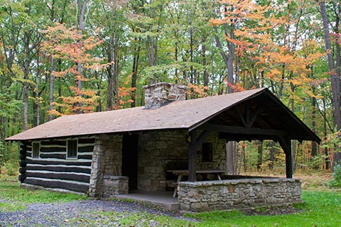 A cozy log and stone cabin is near a forest just starting to turn autumn-colored at Simon B Elliott State Park.