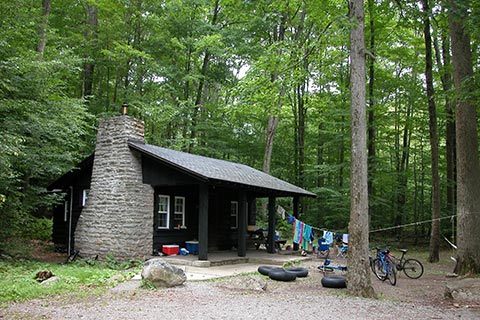 Drying clothes, inner tubes, and parked bikes are near a quaint rustc cabin surrounded by trees at Worlds End State Park. 