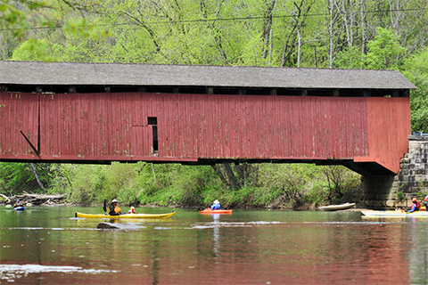A covered bridge spans accross a river with kayakers in the water.