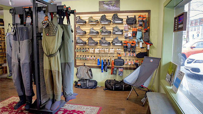 A retail store with fishing gear like waders, boots, and als ocamping gear like chairs. A window lets outside light into the sho