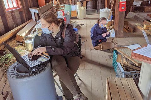 People inside a wooden bulding holding various tools and objects.