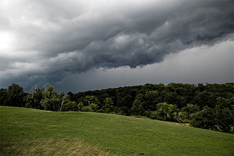 dramatic storm clouds approaching above a green hill