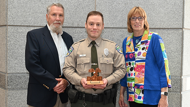 Ranger Ralph Barb stands in between Deputy Secretary John Norbeck and Secretary Cindy Adams Dunn holding wooden award.