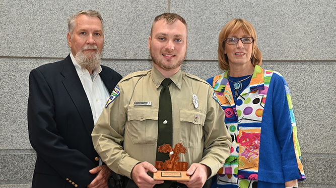 Ranger Troy Baney stands in between Deputy Secretary John Norbeck and Secretary Cindy Adams Dunn holding wooden award