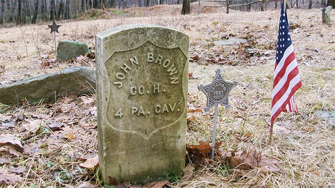 A headstone with the text: john Brown Co. H 4 PA Cav. An american flag sticks in the ground next to it.
