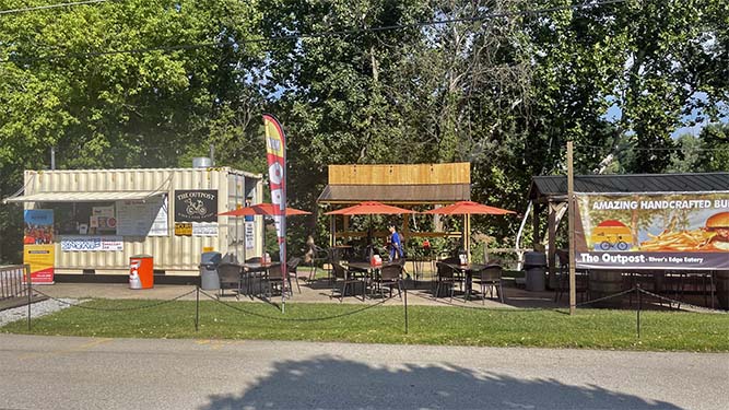 A food truck and two small pavilions along a paved road, with umbrellas and chairs and tables outside.