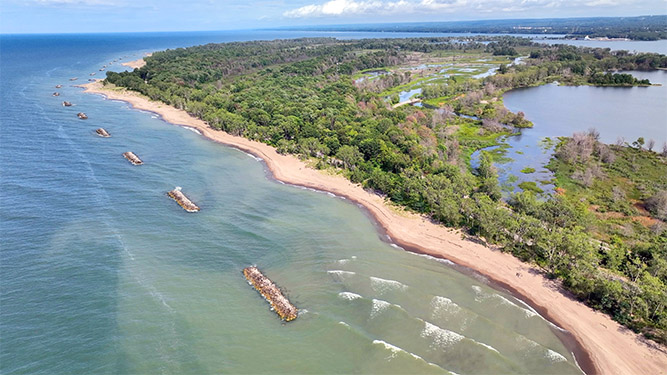 An aerial view of a hook shaped penninsula of wetlands surrounded by sandy beaches.