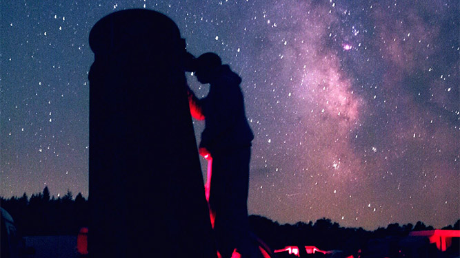 A persons silhouette is seen next t oa large dark shape in front of a starry night sky