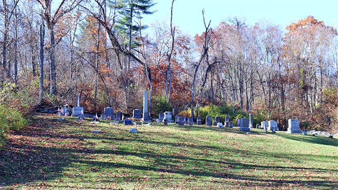 A small cemetery sits on a small hill in front of woodlands during autumn.
