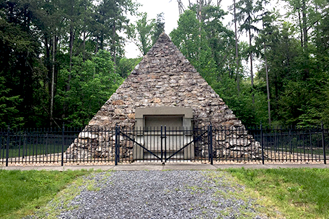 A pryamid stone structure surrounded by a short metal fence in the woods