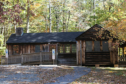 A wood sided building with an accessible ramp in the woods. A stone driveway approaches the cabin.