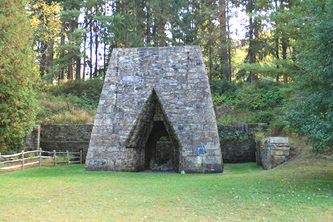 A tall, stone structure outdoors with a triangular opening at the base.