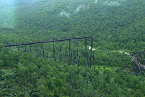 A tall, thin, bridge structure end abruptly as it crosses a wide gorge full of trees.