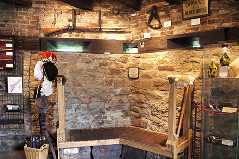 Interior of a stone building with various items hung for display like a rifle, hats, tools, and signs.