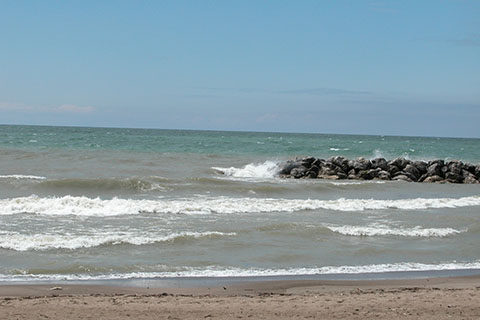 Waves crash onto a beach. S tone jetty sticks out into the water a short ways.