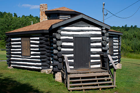 An octagonal log cabin is near a forest at Parker Dam State Park.