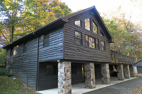 A three story wood sided cabin with rock pillars supporting a walkout bottom floor in the woods.