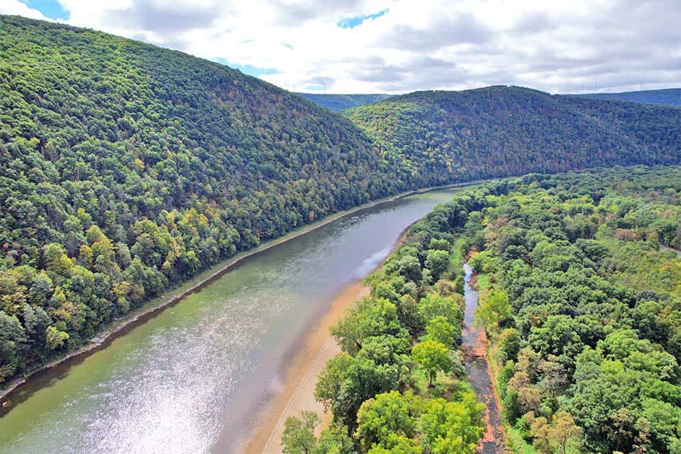 An aerial view of a river as it winds its way past forested mountains and hills.