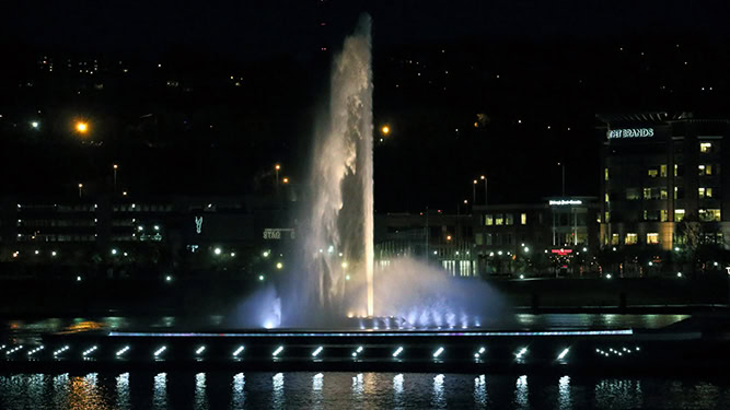 Water fountain shoots water straight up into the air and lit up at night in city